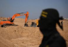 قاتل من «الجهاد الإسلامي» يراقب عمالاً مصريين يحفرون بآلية ثقيلة بحثاً عن جثث المختطفين في النصيرات شمال قطاع غزة الجمعة (أ.ب)