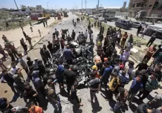 فلسطينيون يتجمَّعون حول سيارة مُدمَّرة بعد استهدافها بغارة إسرائيلية في شارع صلاح الدين جنوب مخيم البريج بقطاع غزة (أ.ف.ب)