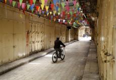 فلسطينيون يمرون من أمام محلات تجارية مغلقة بسبب فيروس كورونا