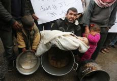 فلسطيني يحمل طفله بغزة احتجاجاً على قطع المساعدات الغذائية- APA Images