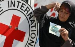 سيدة فلسطينية تحمل صورة أسير وتقف بجانب شعار الصليب الأحمر