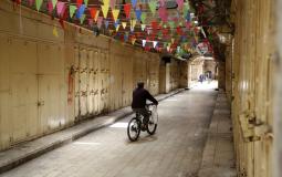 فلسطينيون يمرون من أمام محلات تجارية مغلقة بسبب فيروس كورونا