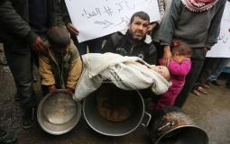 فلسطيني يحمل طفله بغزة احتجاجاً على قطع المساعدات الغذائية- APA Images