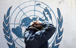 لاجئ يقف أمام شعار وكالة الاونروا في غزة