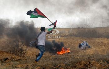 شاب يرفع العلم الفلسطيني خلال المواجهات مع قوات الاحتلال على حدود غزة اليوم