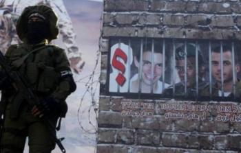 مقاتل من القسام يقف أمام صورة للجنديين الاسرائيليين المحتجزين في غزة