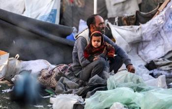 أي يحتضن طفله وسط الدمار في غزة - تعبيرية