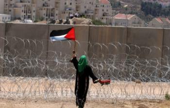 مواطنة فلسطينية تقف أمام جدار فصل في الضفة الغربية