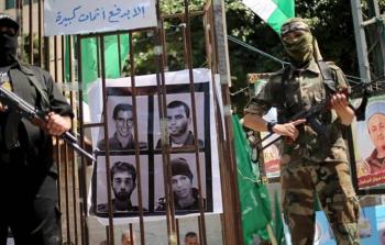 عنصران من القسام يقفان بجانب صورة للأسرى الإسرائيليين لديهم