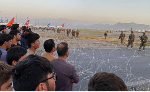 صورة لمواطنين أفغان ينتظرون دورهم في الصعود الى الطائرة مع وجود القوات الأمريكية لحراسة مطار كابول "AFP"