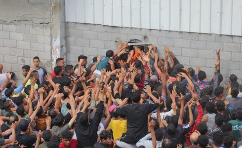 نازحون فلسطينيون يحاولون الحصول على الخبز عبر نافذة مخبز في مخيم النصيرات للاجئين بعد دخول إمدادات الطحين المحدودة إلى قطاع غزة