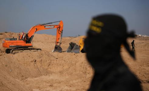قاتل من «الجهاد الإسلامي» يراقب عمالاً مصريين يحفرون بآلية ثقيلة بحثاً عن جثث المختطفين في النصيرات شمال قطاع غزة الجمعة (أ.ب)