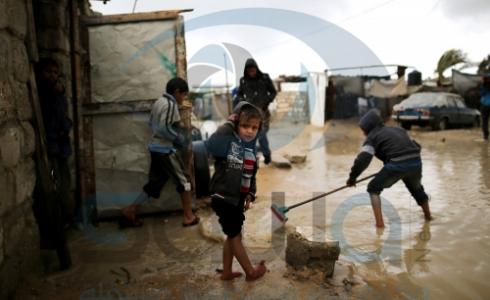 أطفال يحاولون ازاحة المياه من على باب منزلهم