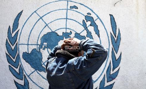 لاجئ يقف أمام شعار وكالة الاونروا في غزة